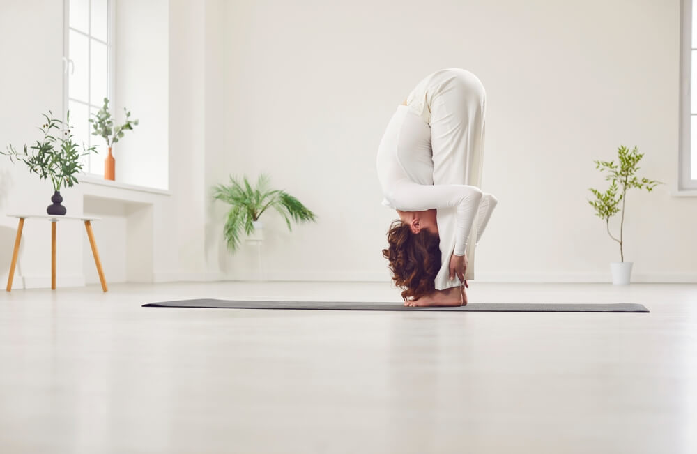 Woman Practicing Uttanasana (Standing Forward Bend) in a Peaceful Yoga Studio Woman Practicing Uttanasana (Standing Forward Bend) in a Peaceful Yoga Studio