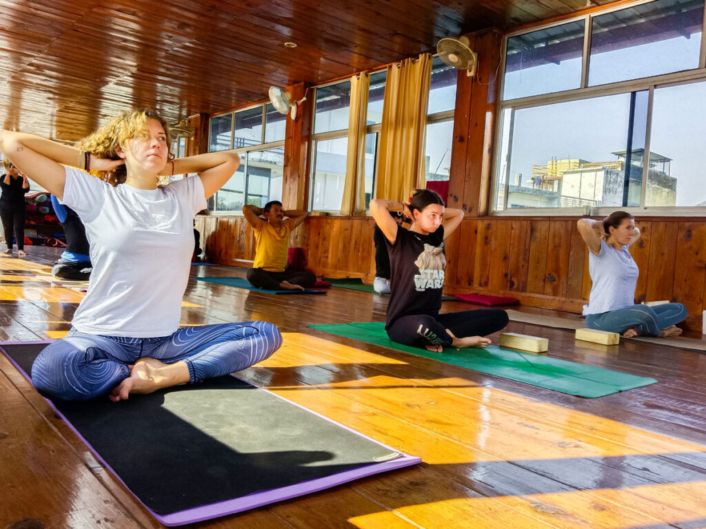 International Yoga Day- Everything You Need To Know! 1 A group of yoga practitioners sitting cross-legged on mats in a wooden yoga hall