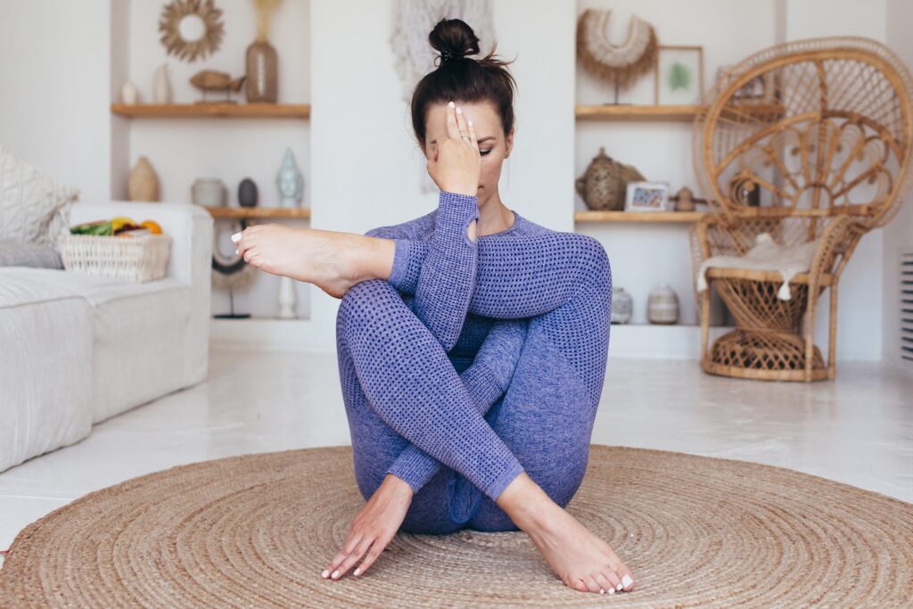 Women Doing Yoga Pose A woman in a blue textured yoga outfit practicing a seated yoga pose in a cozy, bohemian-style living room