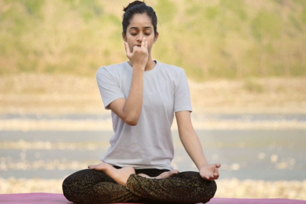 Woman practicing Surya Bhedana Pranayama in a seated position by the riverside, closing one nostril with her hand Woman practicing Surya Bhedana Pranayama in a seated position by the riverside, closing one nostril with her hand